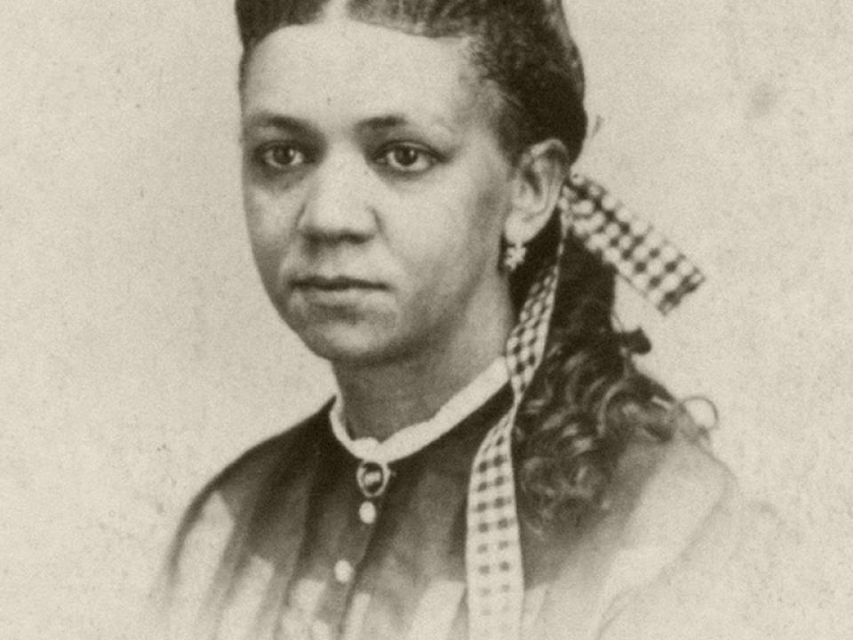 Black and white headshot photo of Fanny Jackson Coppin with hair braided with gingham ribbon while also wearing a button up blouse