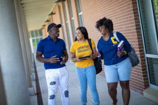 Three students chat as they walk under an outdoor walkway